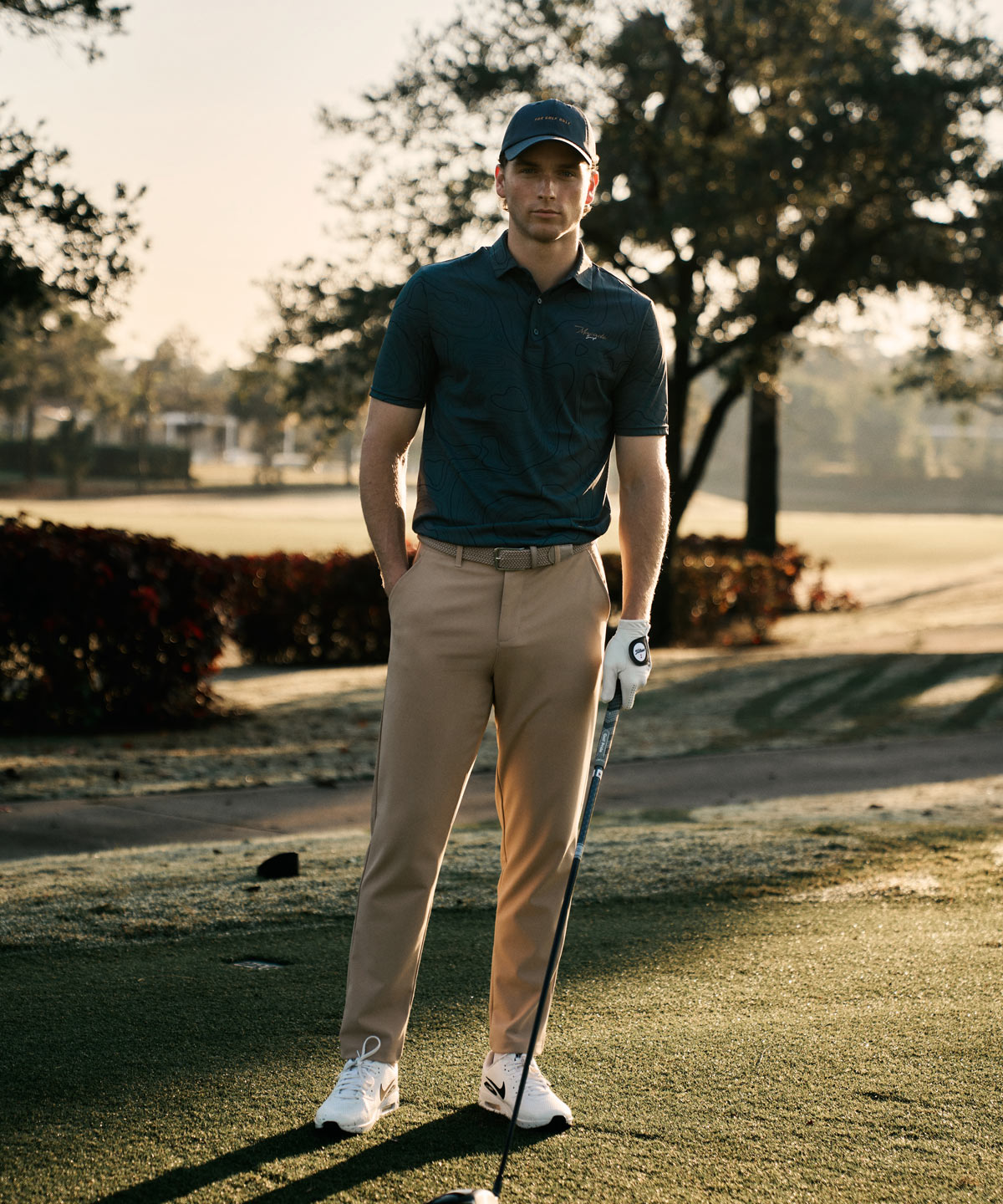 Men’s sand Links Tech Trouser styled on the golf course with a dark polo, cap, and golf glove, highlighting the tailored fit and versatile design for both performance and everyday wear.