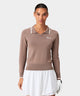Front view of a woman wearing the Ella Knit Top in taupe, featuring a long sleeve design with contrast tipping on the collar and cuffs, sleek Macade logo at the left chest, and paired with a white golf skort and glove for a polished, athletic golf look.