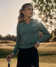 Woman on a golf course at sunset wearing the sage green Ella Knit Top with white contrast tipping at the collar and cuffs, paired with a black skort, holding a putter.