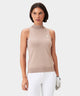 Woman wearing a tan Kayla Air Sleeveless Top with a high mock neck and ribbed hem, paired with white golf pants and a glove for a clean, modern golf look.