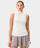 Woman wearing a white Kayla Air Sleeveless Top with a high mock neck, ribbed hem, and subtle chest logo, paired with a light taupe golf skirt and a white golf glove for a clean, modern golf look.