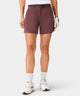 Woman wearing mauve Macade Golf Flex Shorts with a high-waisted, athletic fit, styled with a woven belt, golf glove, and white sneakers for a modern, performance-ready look. The shorts feature deep side pockets and a clean, tailored silhouette, ideal for both golf and everyday versatility.
