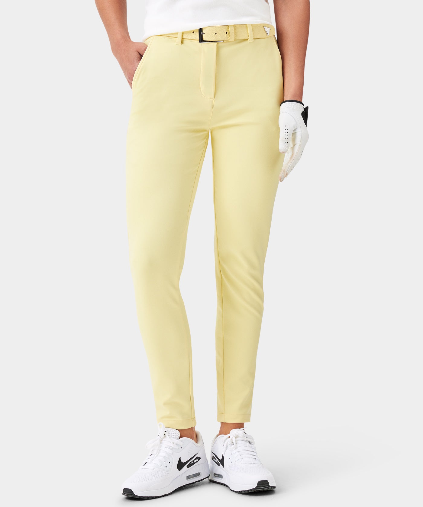 Woman wearing the Women's Tour Belt in lemon yellow, styled with matching yellow golf pants, a white top, and golf glove, showcasing the belt's pebbled leather front, elastic woven strap, and sleek buckle for a coordinated, modern golf outfit.