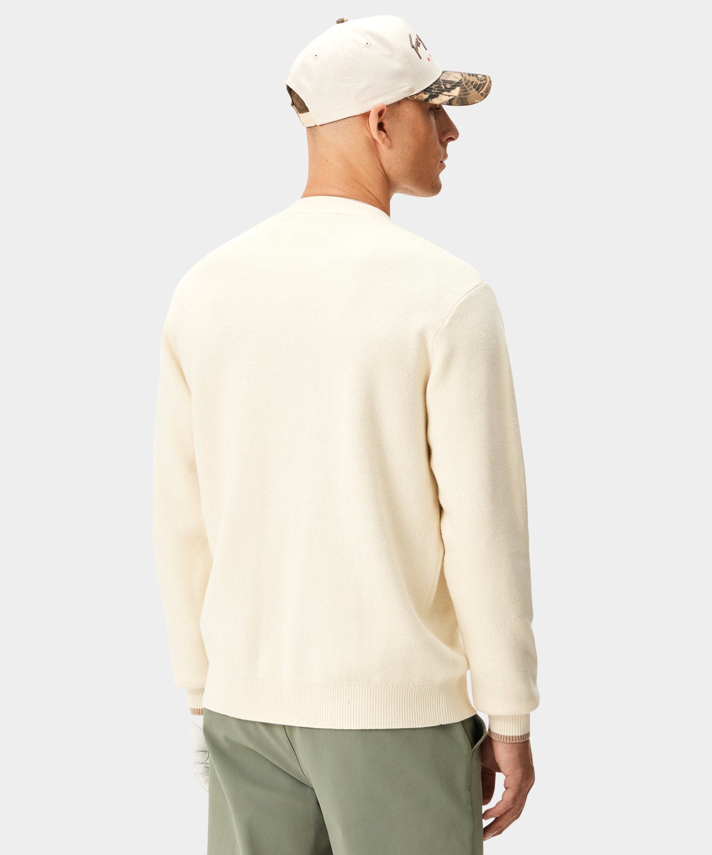 Man wearing the Macade Golf Two-Tone Script Snapback in a light colorway with a camo underbrim, styled with an off-white sweater and sage green pants for a clean, modern golf look.