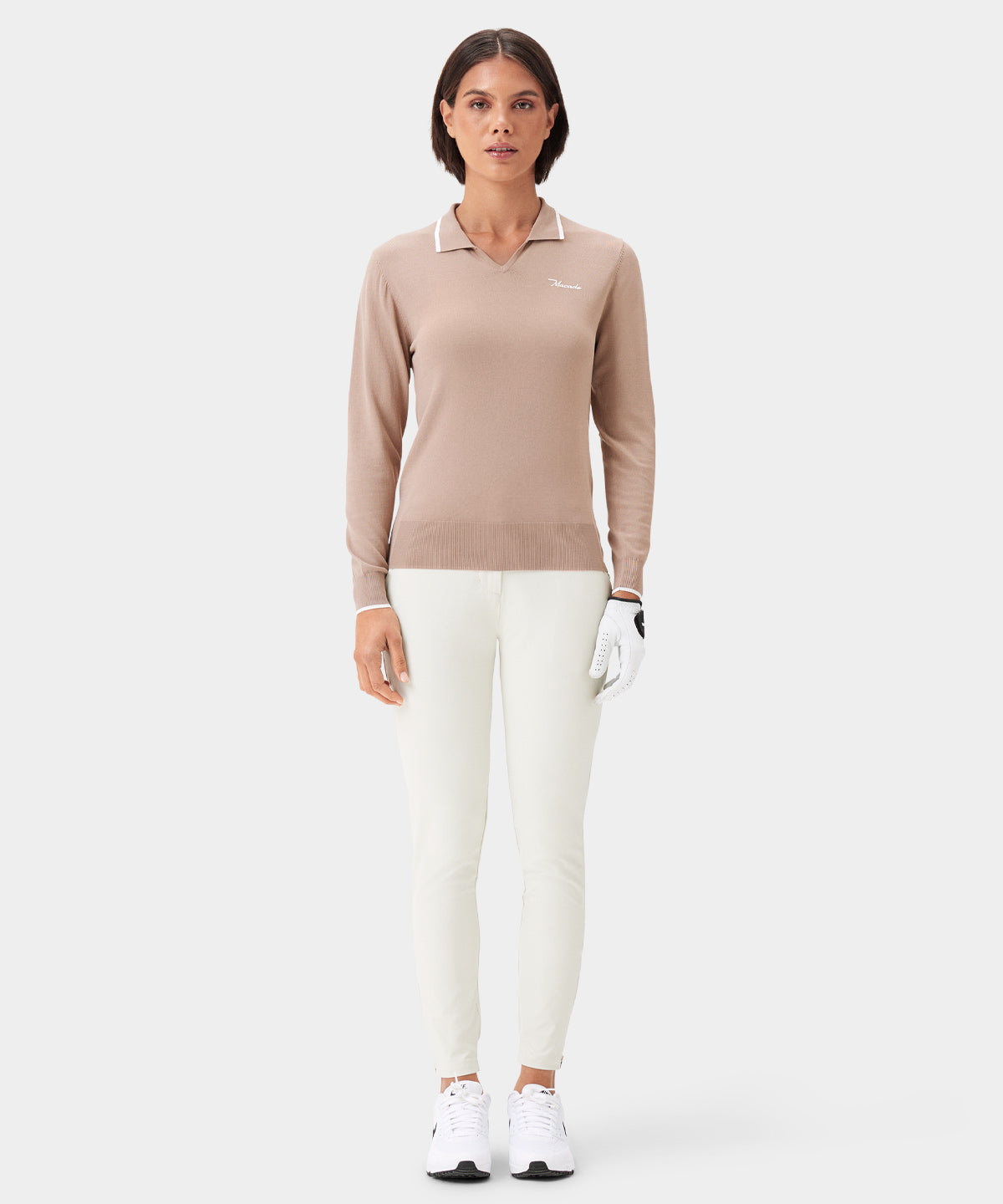 Woman wearing the Ella Knit Top in taupe, featuring long sleeves, a contrast-tipped collar, and a minimal Macade logo at the left chest, styled with white golf pants, white sneakers, and a golf glove for a sophisticated, performance-ready look.