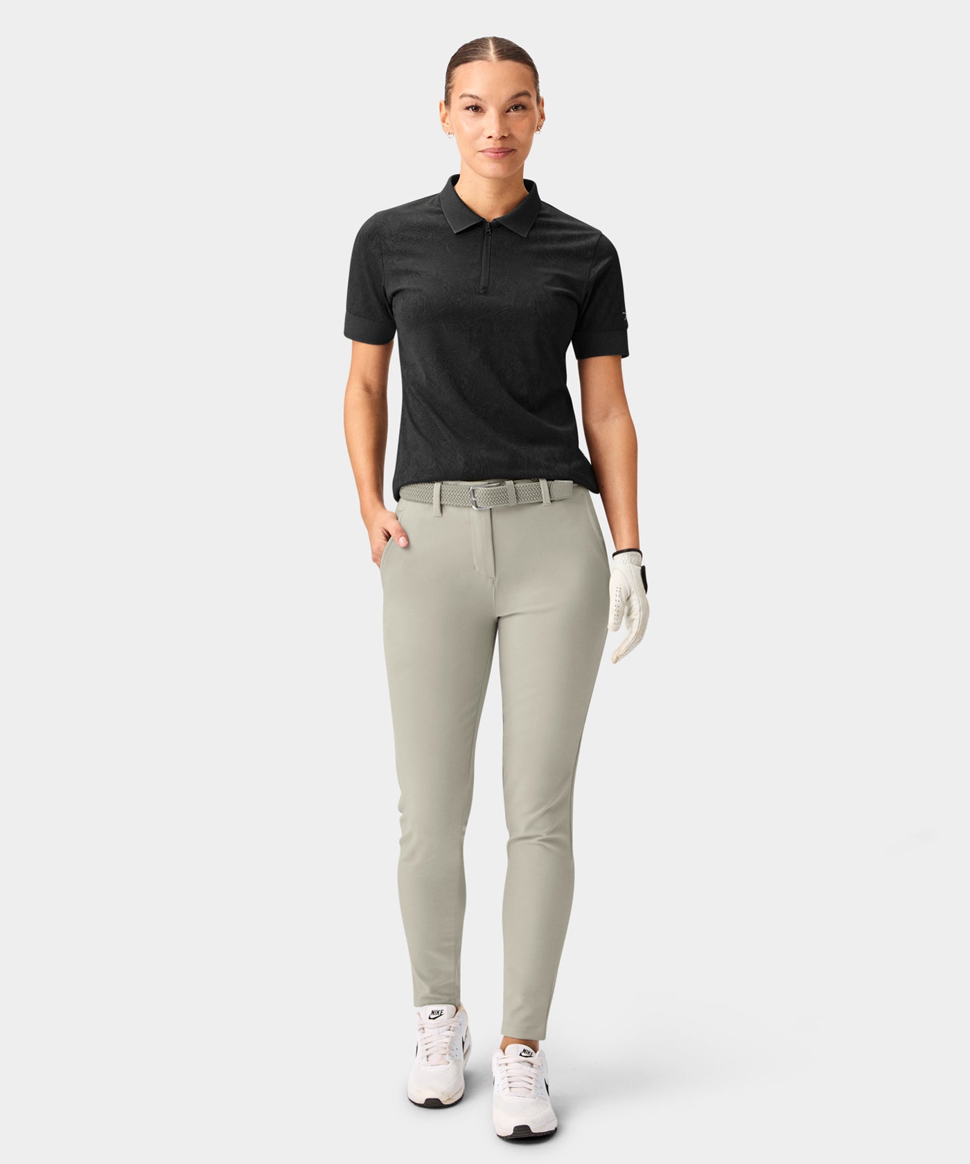 Woman wearing Macade Golf Performance Trouser in light grey, styled with a black polo and golf glove, highlighting the straight, ankle-length fit, deep front pockets, and smooth technical fabric designed for comfort and versatility on and off the course.