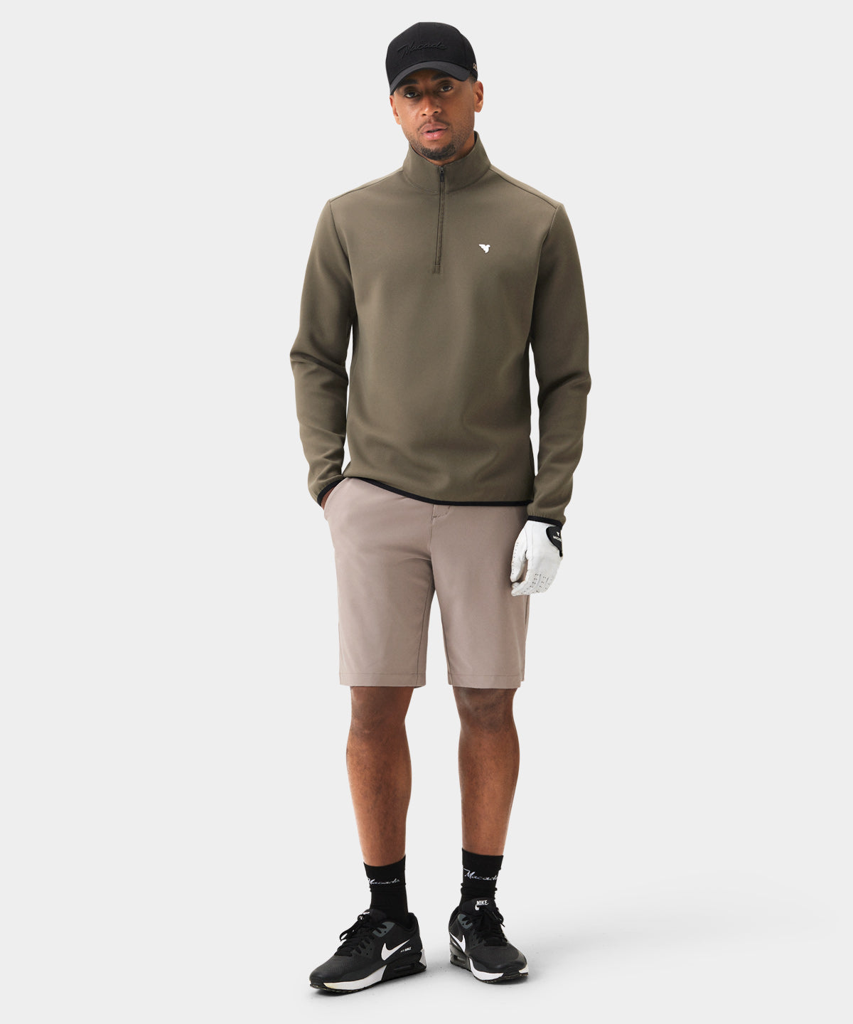 Male golfer wearing the Macade Golf Therma Quarter Zip in olive green, styled with neutral shorts, black sneakers, and a golf glove, showcasing the sweater’s minimalist design, sleek tonal trims, and tailored athletic fit for a refined, versatile look on and off the course.