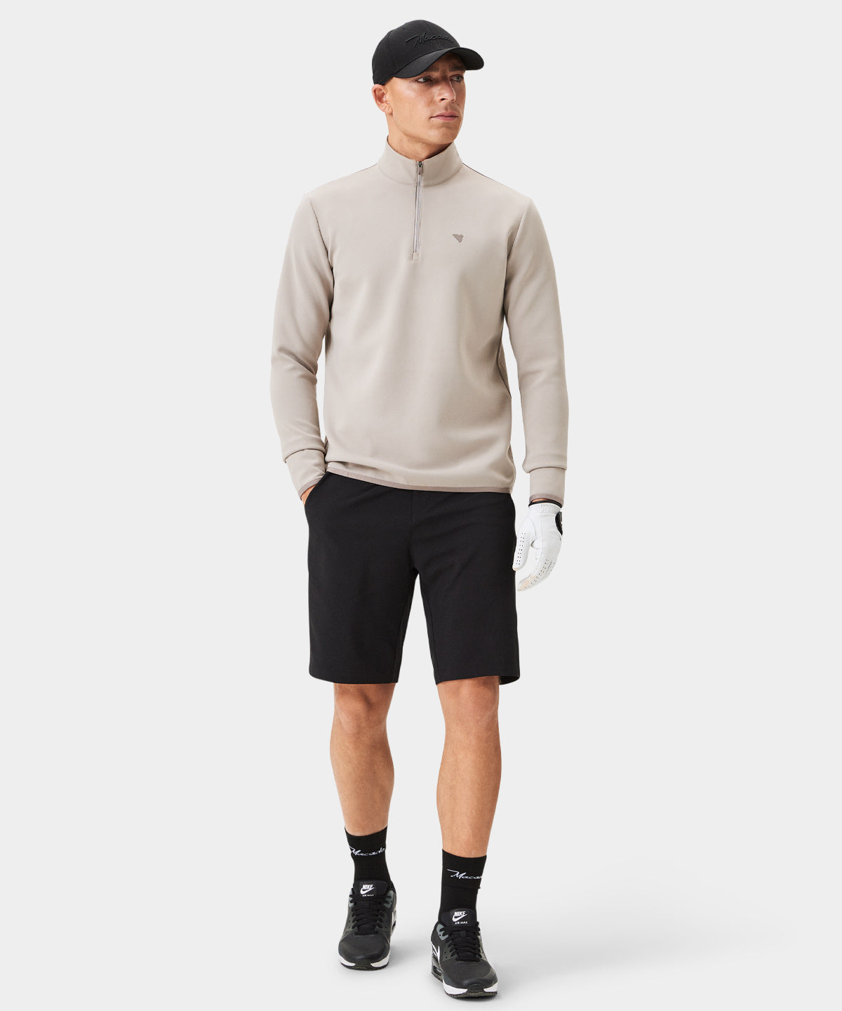 Man wearing a taupe Macade Golf Therma Quarter Zip with a minimalist tonal chest logo, paired with black golf shorts, black sneakers, and a black cap, highlighting the sweater’s clean, modern fit and versatile style for golf and everyday wear.