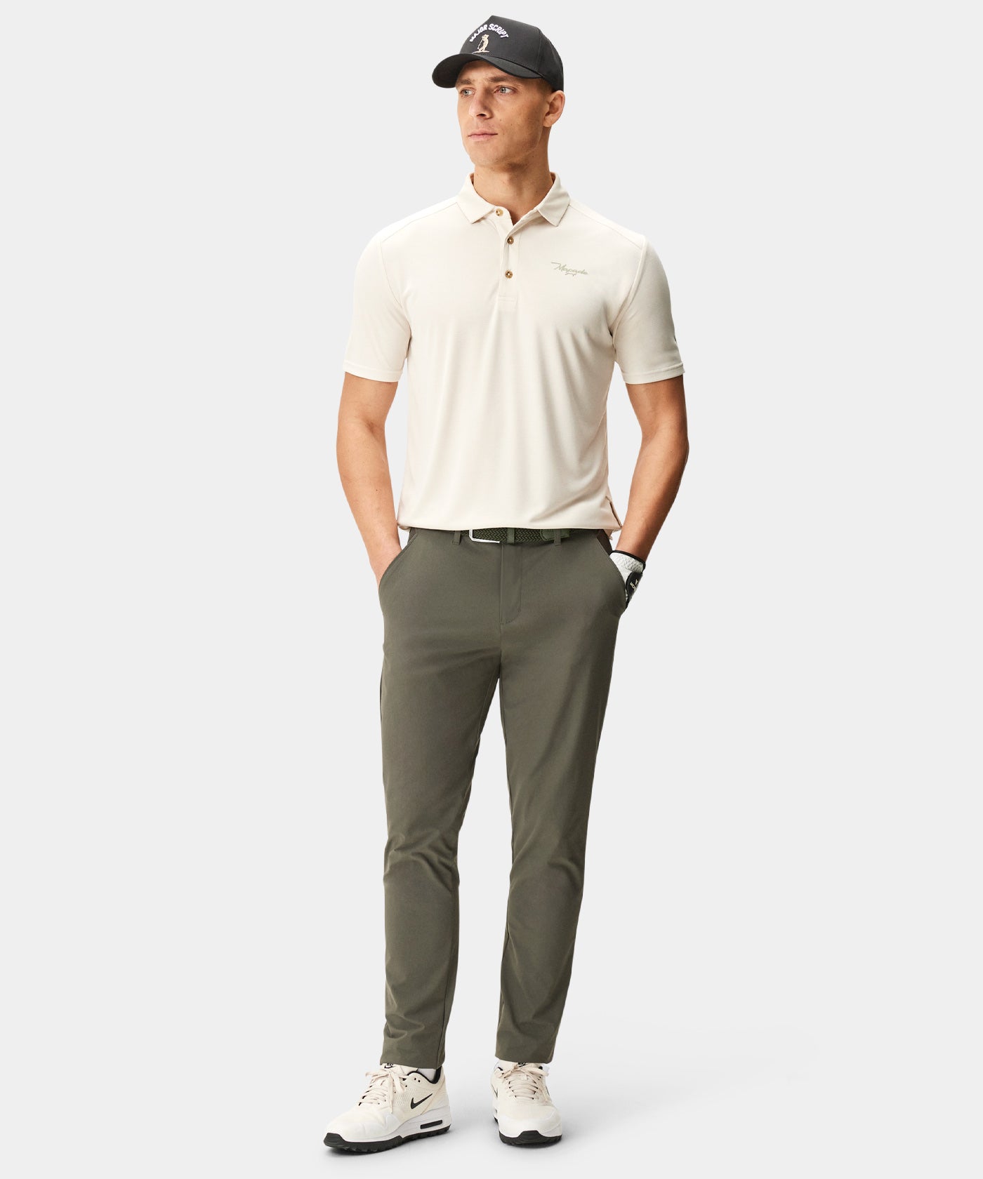 Man wearing Macade Golf Lightweight Trouser in moss green, styled with a cream polo, golf glove, and cap, highlighting the slim, tapered fit and versatile design for both golf and everyday wear.