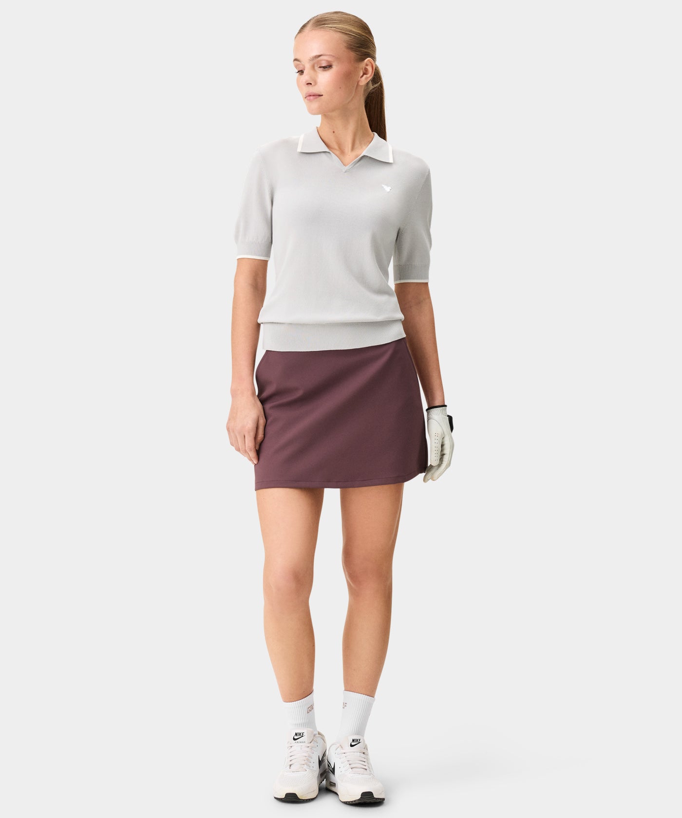 Woman wearing the TX Air Skirt in mauve, styled with a light short-sleeve polo and golf shoes, showcasing the skirt’s clean drape, wide waistband, and minimal, modern silhouette designed for comfort and performance on and off the course.
