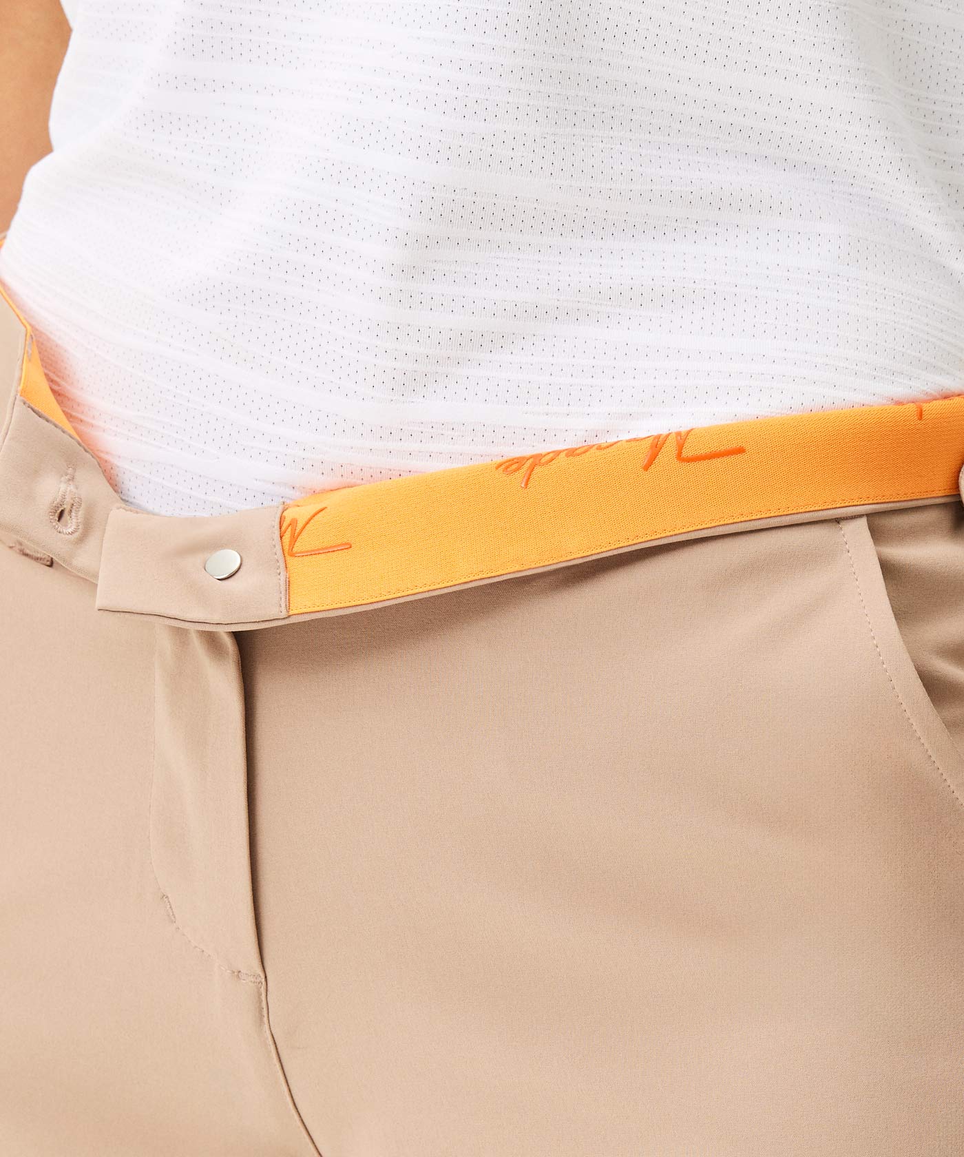 Close-up of Macade Golf Flex Shorts in tan, featuring a secure snap closure, deep side pocket, and a vibrant orange inner waistband, paired with a lightweight white golf top for a fresh, athletic style.