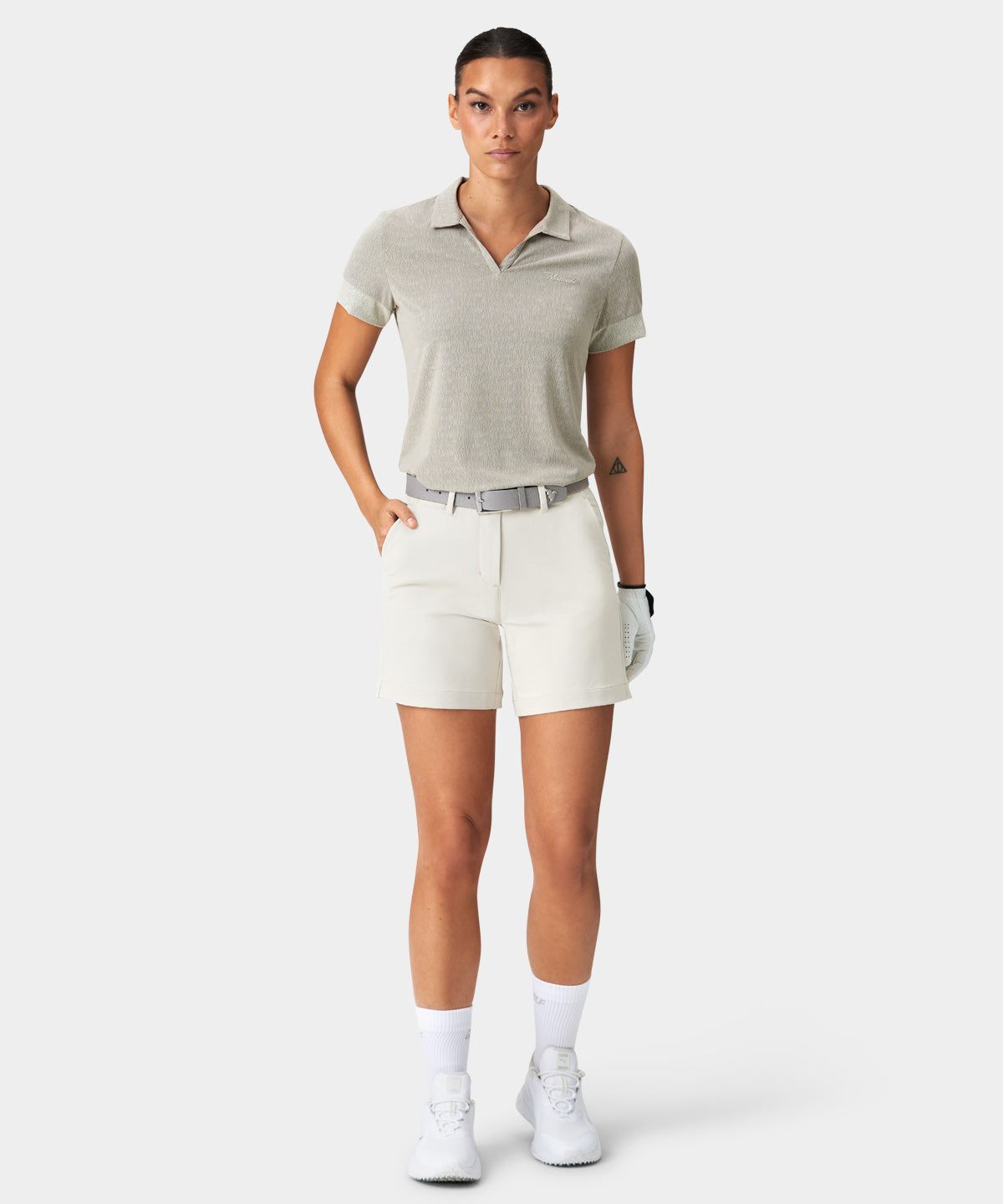 Model wearing Macade Golf Flex Shorts in ivory, paired with a light grey polo shirt, matching belt, and golf glove, highlighting the high-waisted, athletic fit and clean, tailored design for versatile golf and everyday style.