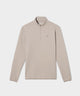Golfer wearing a palm beige Macade Golf Therma Quarter Zip with a minimalist design, subtle chest logo, and tailored fit, styled over a white polo and paired with matching beige pants and a golf glove on a green fairway.