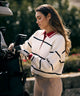 Woman wearing the Club women’s golf sweater in white with navy horizontal stripes, featuring a bold red polo collar and ribbed cuffs, styled with beige pants and a golf glove while placing a club into a golf bag for a refined, sporty on-course look.