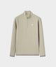 Man wearing a palm beige Macade Golf Therma Quarter Zip with a minimalist white chest logo, carrying a golf bag outdoors, highlighting the sweater’s refined fit and versatile style for on-course performance in cool weather.