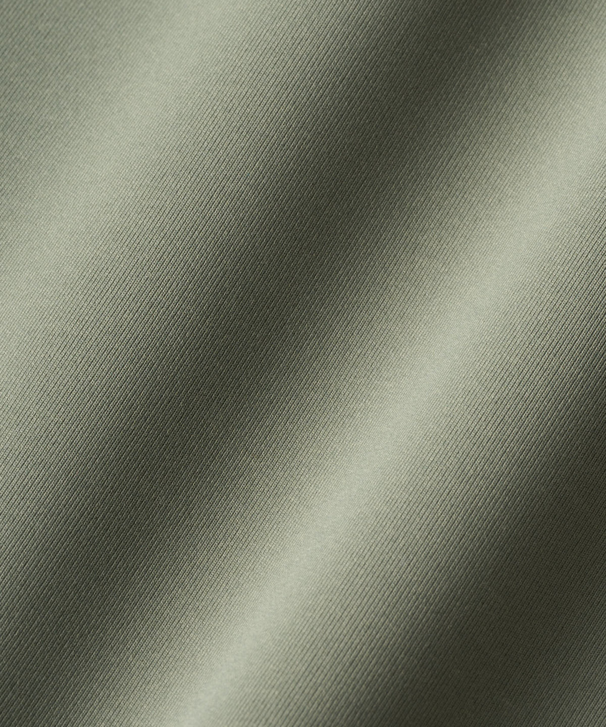 Macro shot of the Therma Zip Hoodie fabric in sage green, showcasing its smooth, matte texture and tightly woven, premium polyester-spandex blend.