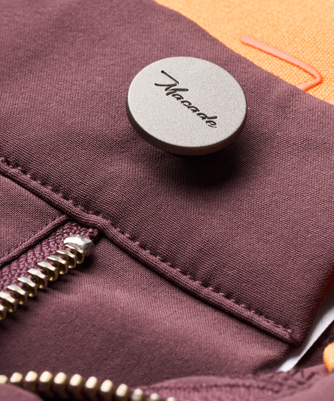 Detail shot of the Macade Golf Four-Way Stretch Shorts in burgundy, highlighting the premium metal button with Macade branding, smooth zipper, and soft, structured fabric.