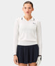 Woman wearing the Ella Knit Top in white, a long sleeve women's golf polo with a contrast-tipped open placket collar and sleek Macade logo at the chest, styled with a black skort and golf glove on a golf course. The fine knit texture and tailored fit highlight its refined, modern look for both on-course and off-course wear.