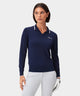 Woman wearing the Ella Knit Top in dark blue with white contrast tipping and a sleek Macade logo at the chest, styled with a white golf skort and carrying a golf bag outdoors.