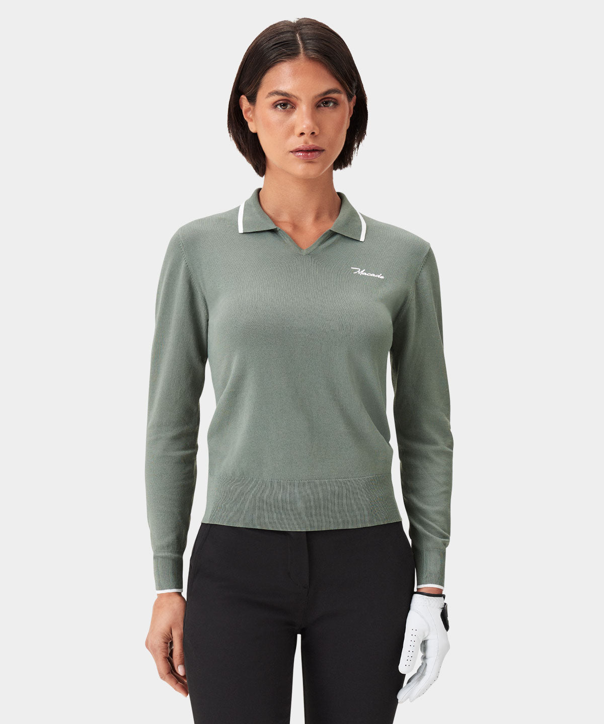 Woman wearing the Ella Knit Top in sage green with white contrast tipping and a minimal Macade logo, paired with black golf pants and a glove for a sophisticated, modern golf outfit.