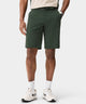 A man wears dark green Macade Golf Four-Way Stretch Shorts with a tailored, above-the-knee fit, styled with a woven belt, golf glove, and white sneakers for a refined, athletic look on and off the course.