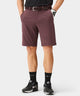 A golfer wears Macade Golf Four-Way Stretch Shorts in a rich burgundy color, featuring a tailored, above-the-knee fit with belt loops and side pockets, styled with a braided belt, black golf socks, and black Nike sneakers for a modern, athletic look.