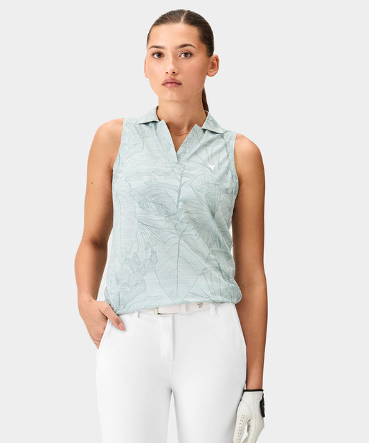 Woman wearing a green palm Paige Sleeveless Shirt by Macade with a subtle leaf print, mock neck, and minimal branding, paired with white golf pants and a white belt for a fresh, modern golf look.