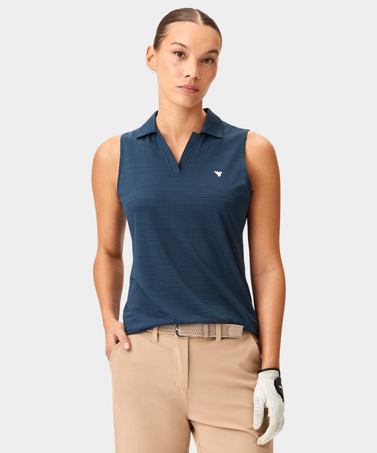 Woman wearing a steel blue Paige Sleeveless Shirt by Macade with a mock neck and minimal branding, paired with beige golf pants and a woven belt for a polished, modern golf look.