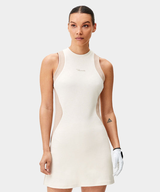 Woman wearing the Macade Golf Inez Sleeveless Dress in cream with tonal mesh side panels, featuring a fitted, athletic silhouette and subtle branding, designed for lightweight comfort and modern golf style.