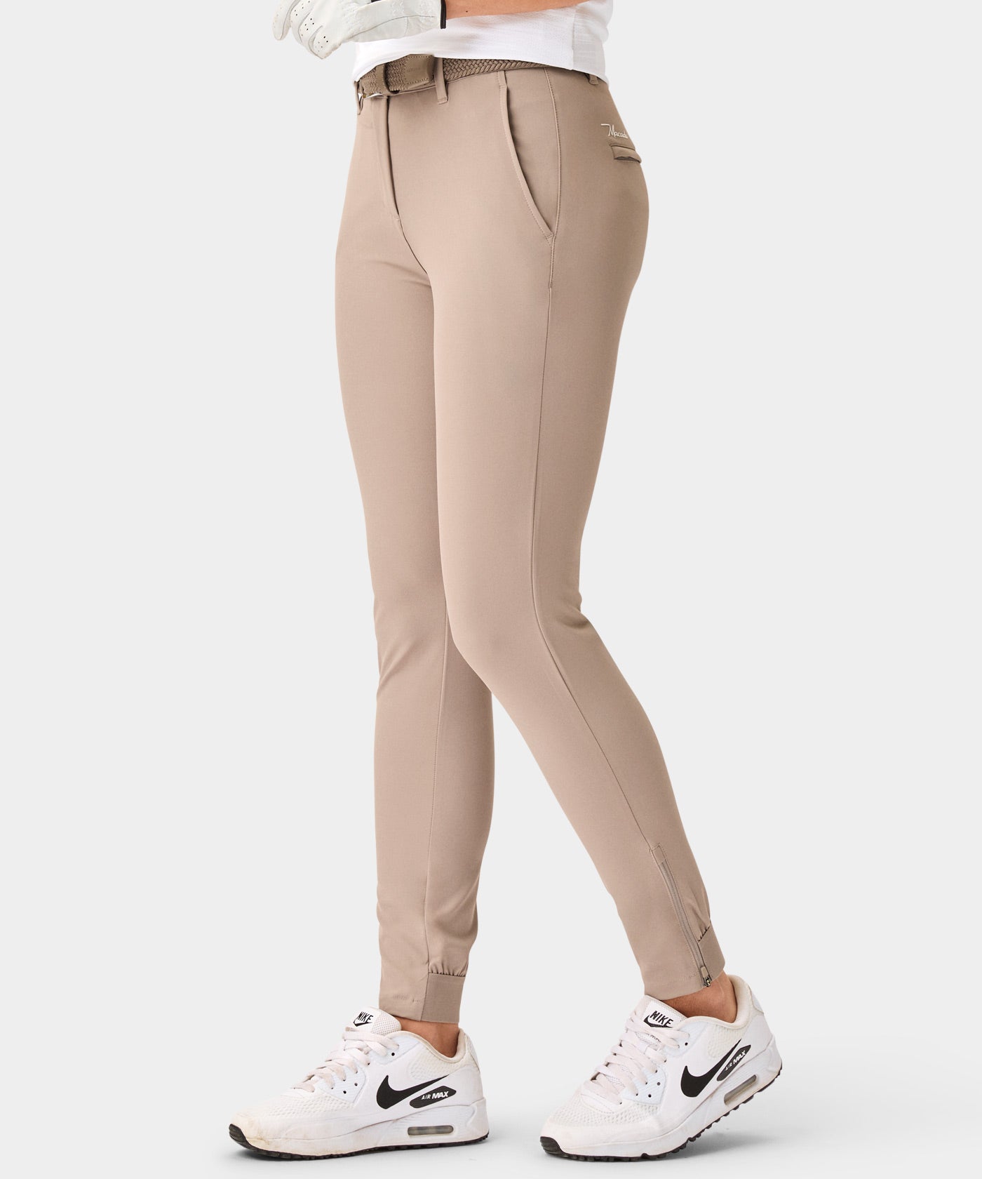 Macade Golf Four-Way Stretch Jogger in bone white, shown with a woven belt and white Nike sneakers, features a slim, ankle-length cut with zippered cuffs and deep pockets for a modern, functional golf style.