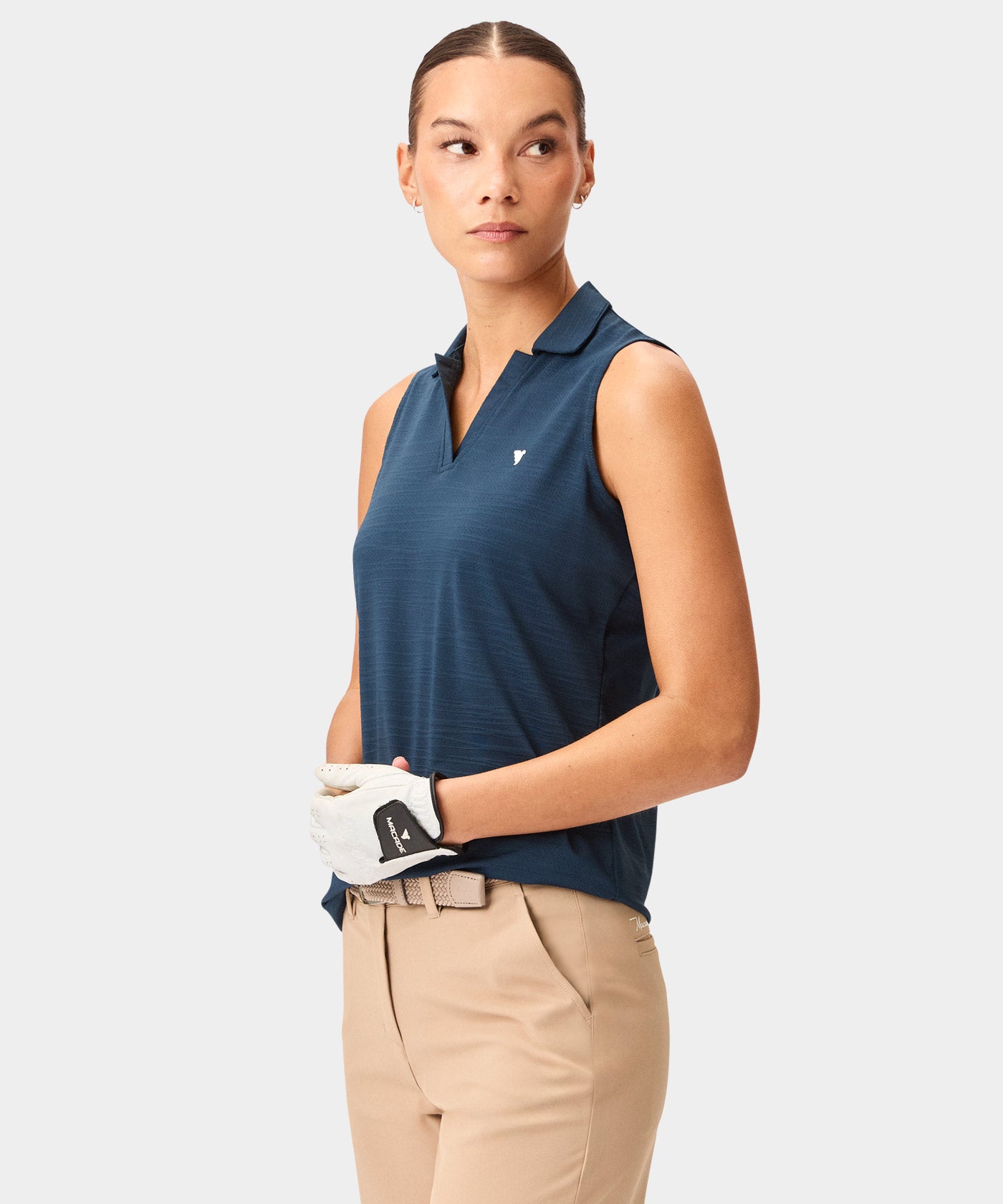 Woman wearing a steel blue Paige Sleeveless Shirt by Macade with a mock neck and minimal branding, paired with beige golf pants and a white golf glove for a refined, athletic style on the course.