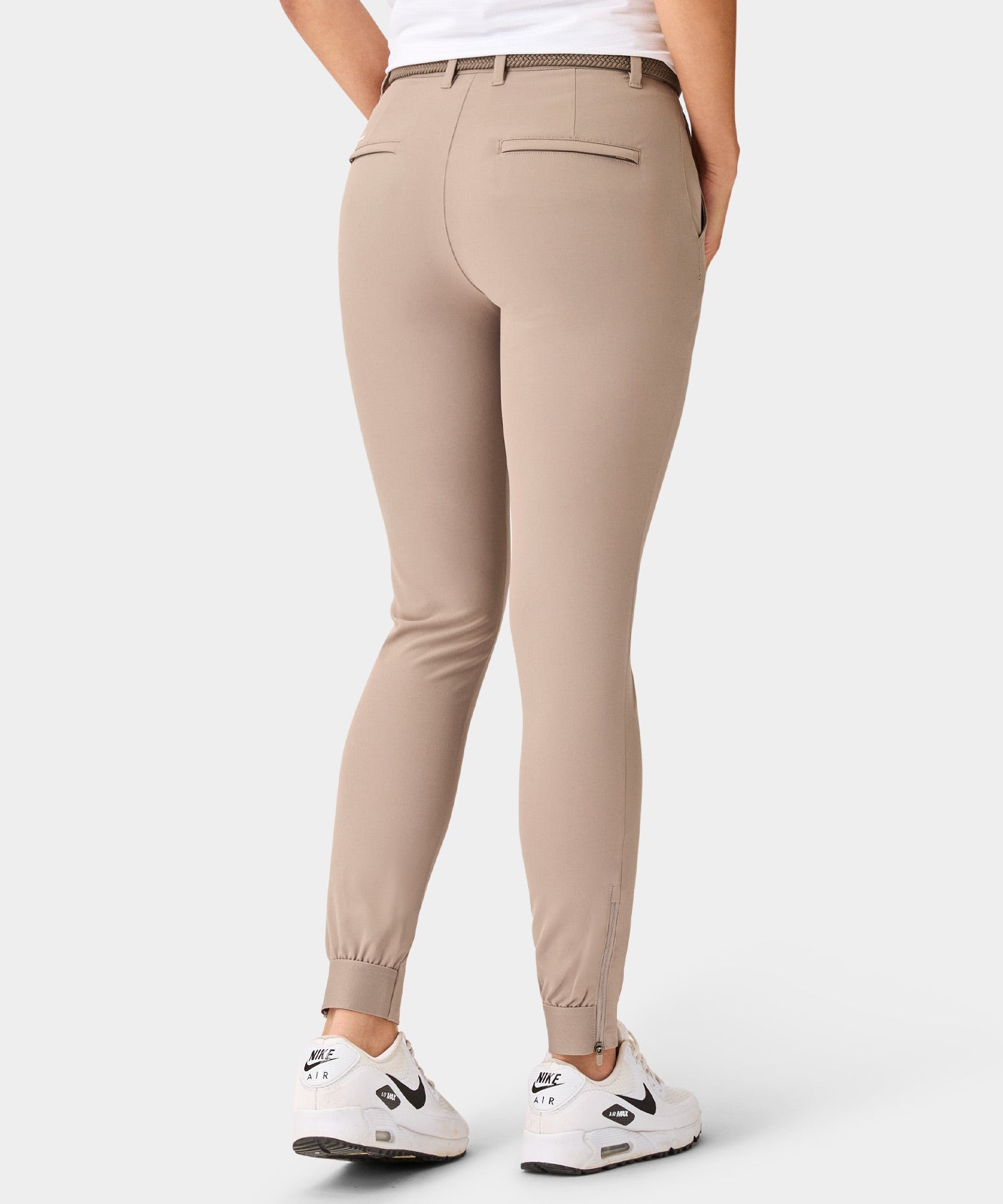 Back view of the Macade Golf Four-Way Stretch Jogger in bone white, featuring a tailored fit, elastic ankle cuffs with zippers, and welt back pockets, styled with a woven belt and white Nike sneakers for a modern golf look.