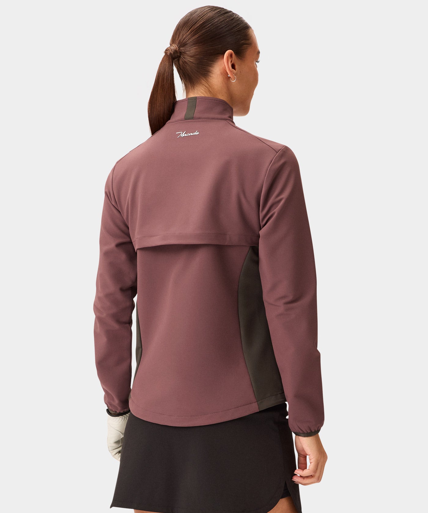 Back view of a woman wearing the Macade Golf Storm Wind Jacket in mauve with dark olive side panels, showcasing the rear ventilation flap, minimal branding, and tailored fit styled for golf.