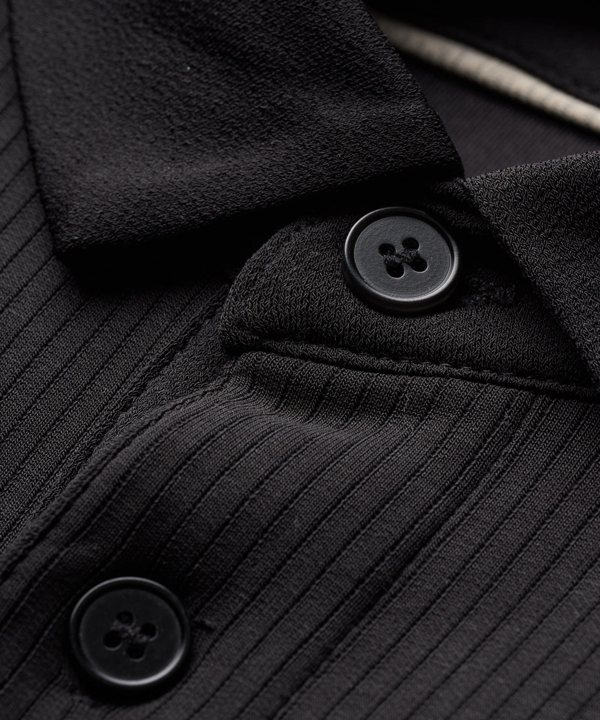 Close-up of the AR Tech Polo’s black ribbed knit fabric, highlighting the soft texture, three-button placket, and refined collar construction for a modern, performance-driven golf shirt.
