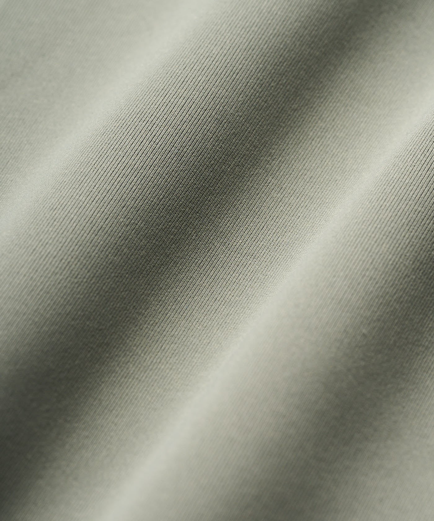 Macro detail of the Macade Therma Vest in Sage Green, showcasing the smooth, tightly woven technical fabric with a soft, refined texture.