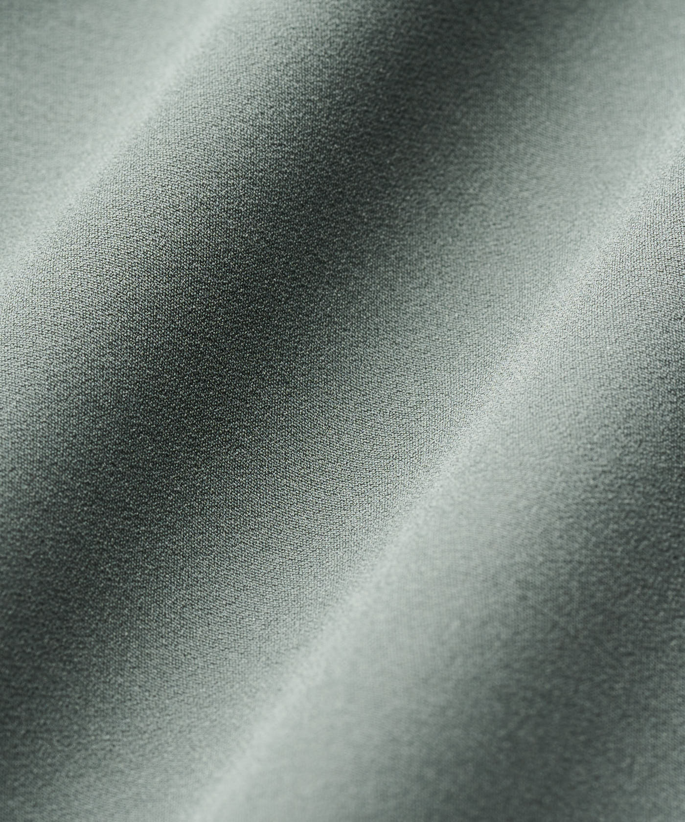 Close-up of the Shell Jacket’s Juniper Green fabric, showcasing the smooth, matte polyester-spandex blend with a soft, flexible drape and refined texture.