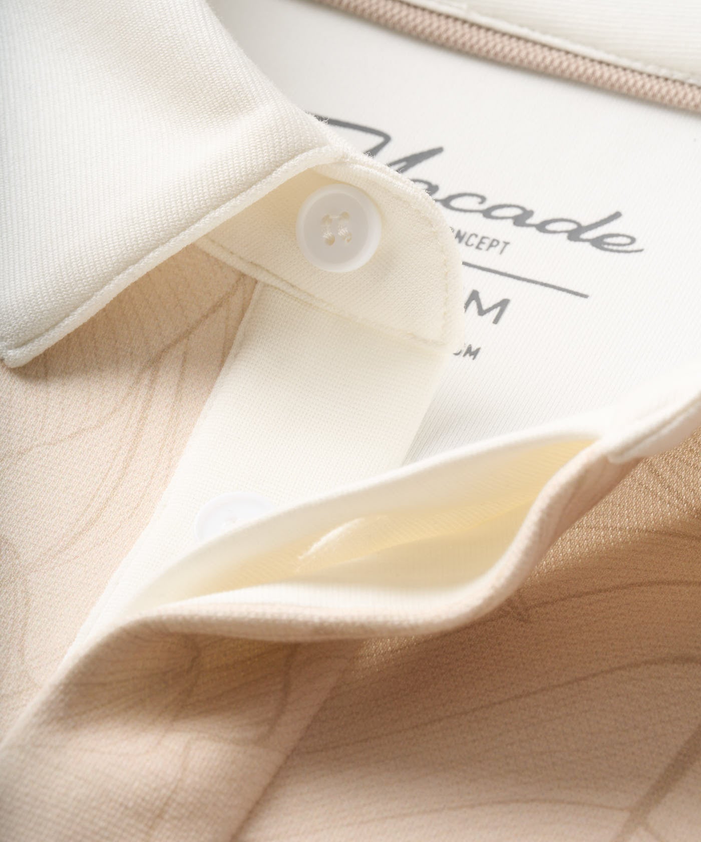 Detail of the Blades Polo Sweatshirt in Palm Beige, showcasing the soft textured jersey fabric with a subtle leaf pattern, crisp white collar, and clean button closure for an elevated, modern look.